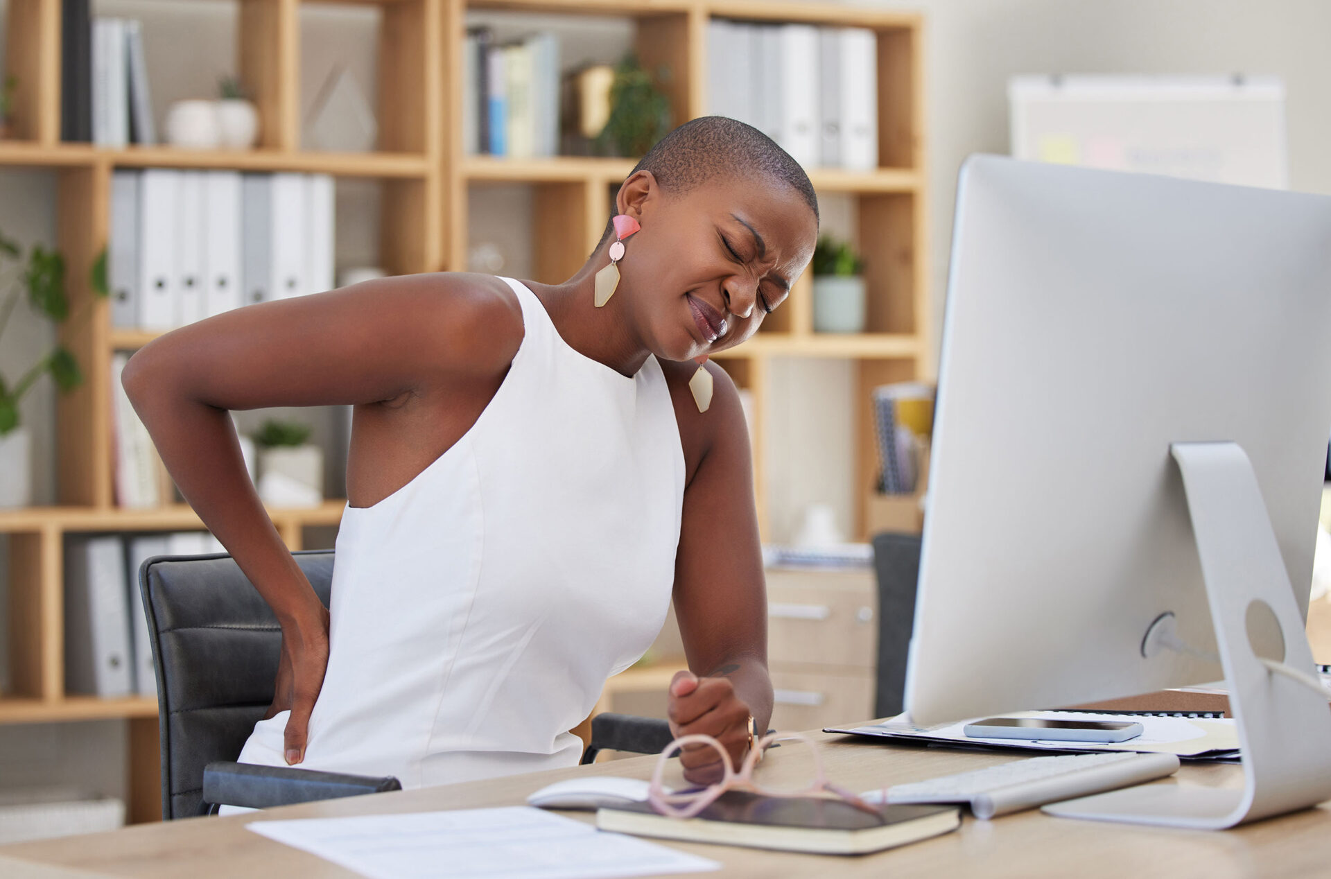 A woman experiencing muscle tension in her back at a desk job.