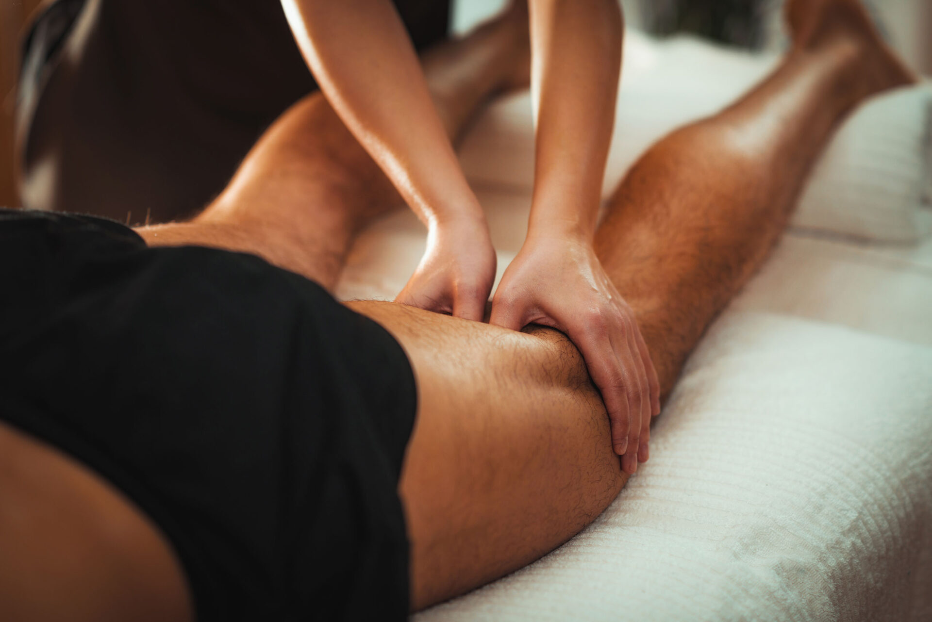 A close-up of a focused therapeutic massage targeting a man's hamstring muscle.